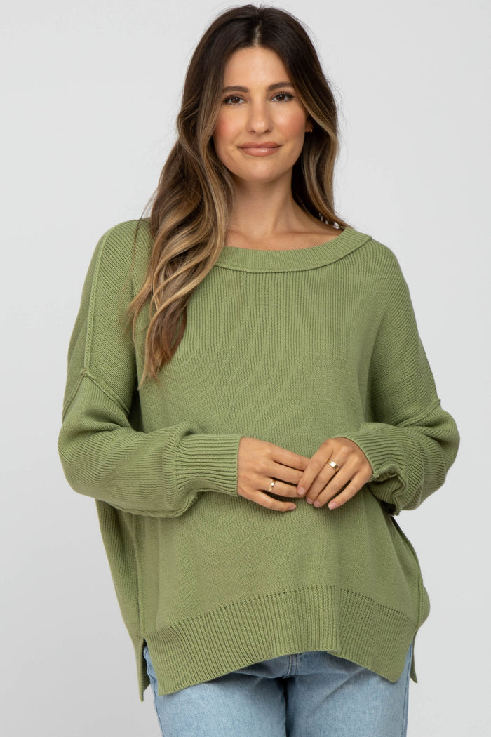 woman wearing a light green oversized maternity sweater with a boat neckline and side slits, holding her baby bump