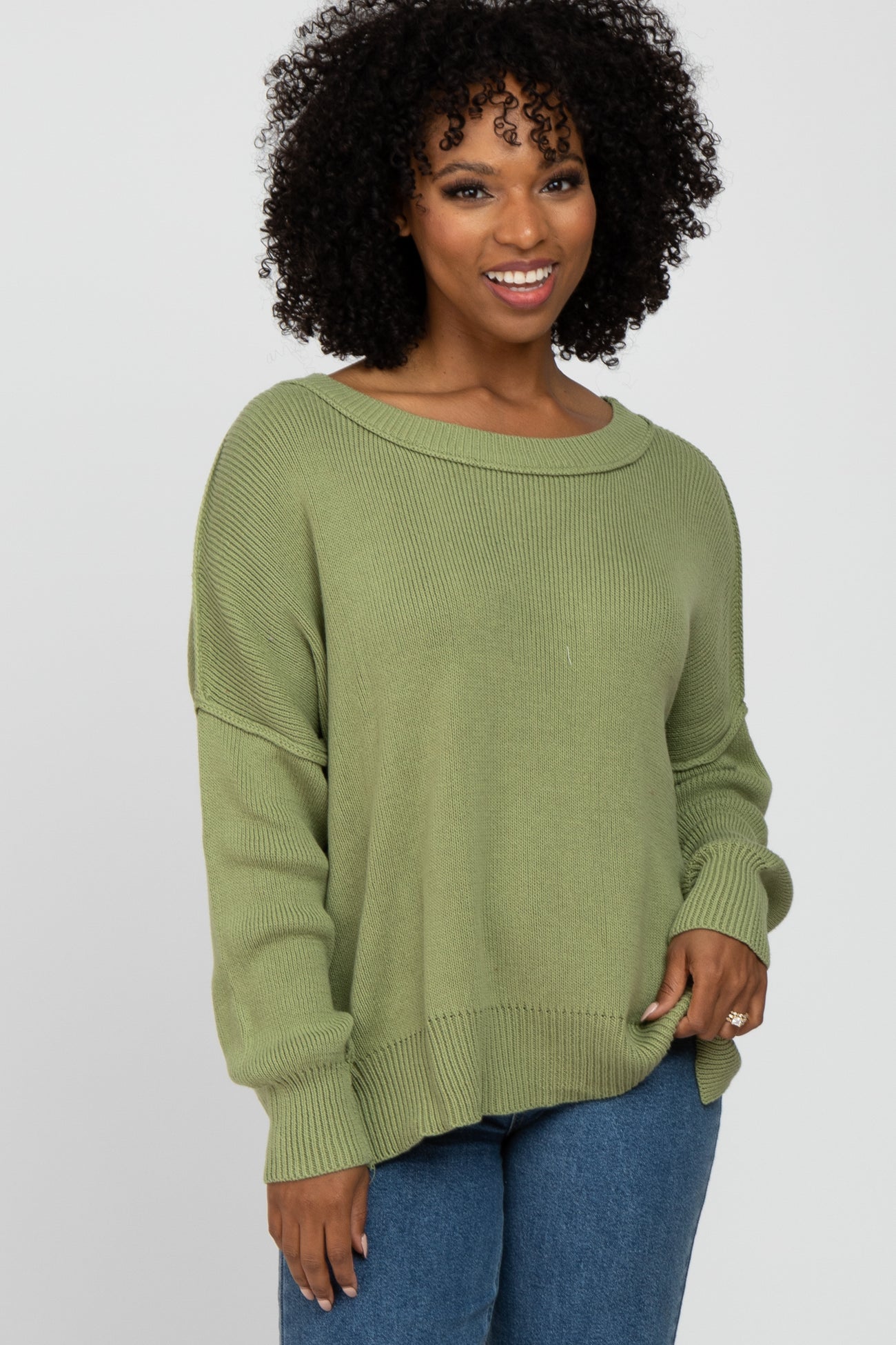 woman wearing a light olive green oversized sweater with a boat neckline and fitted ribbed cuffs