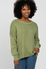 woman wearing a light olive green oversized sweater with a boat neckline and fitted ribbed cuffs