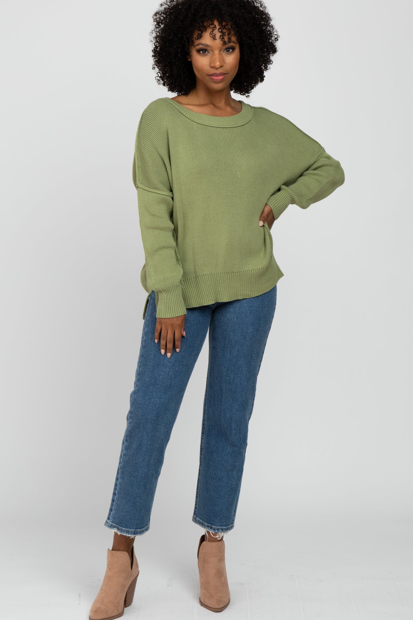 woman wearing a loose-fitting olive green sweater and high-waisted blue jeans with brown ankle boots