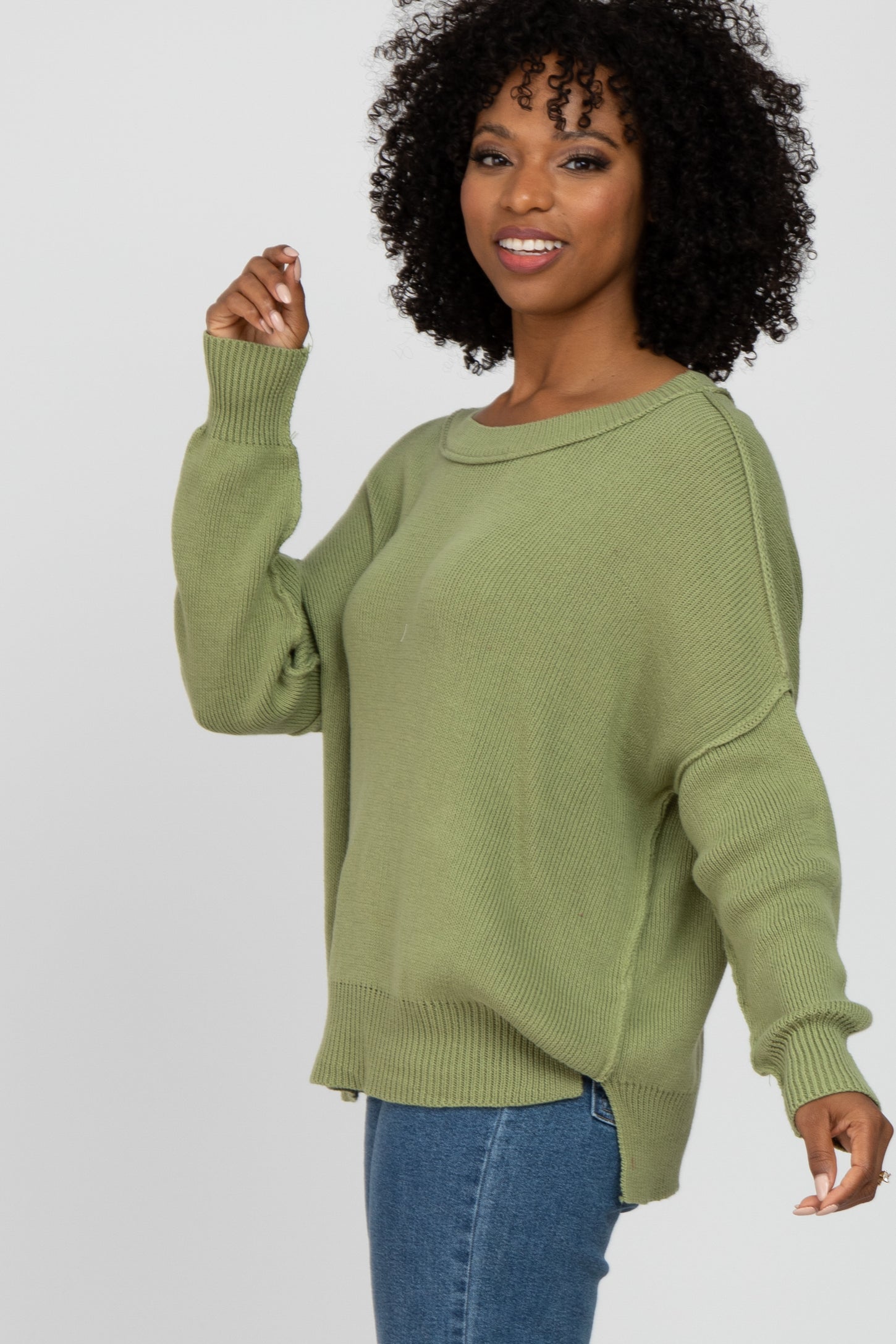 woman wearing an olive green oversized knit sweater and jeans, smiling and posing sideways