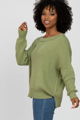 woman wearing an olive green oversized knit sweater and jeans, smiling and posing sideways