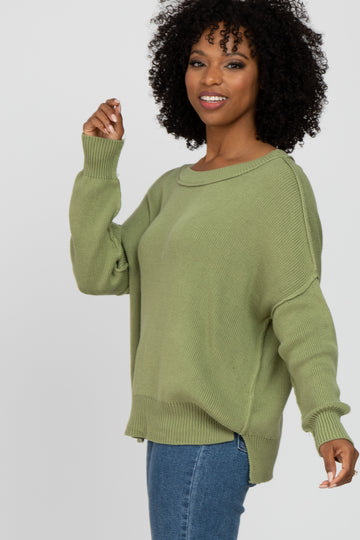 woman wearing an olive green oversized knit sweater and jeans, smiling and posing sideways