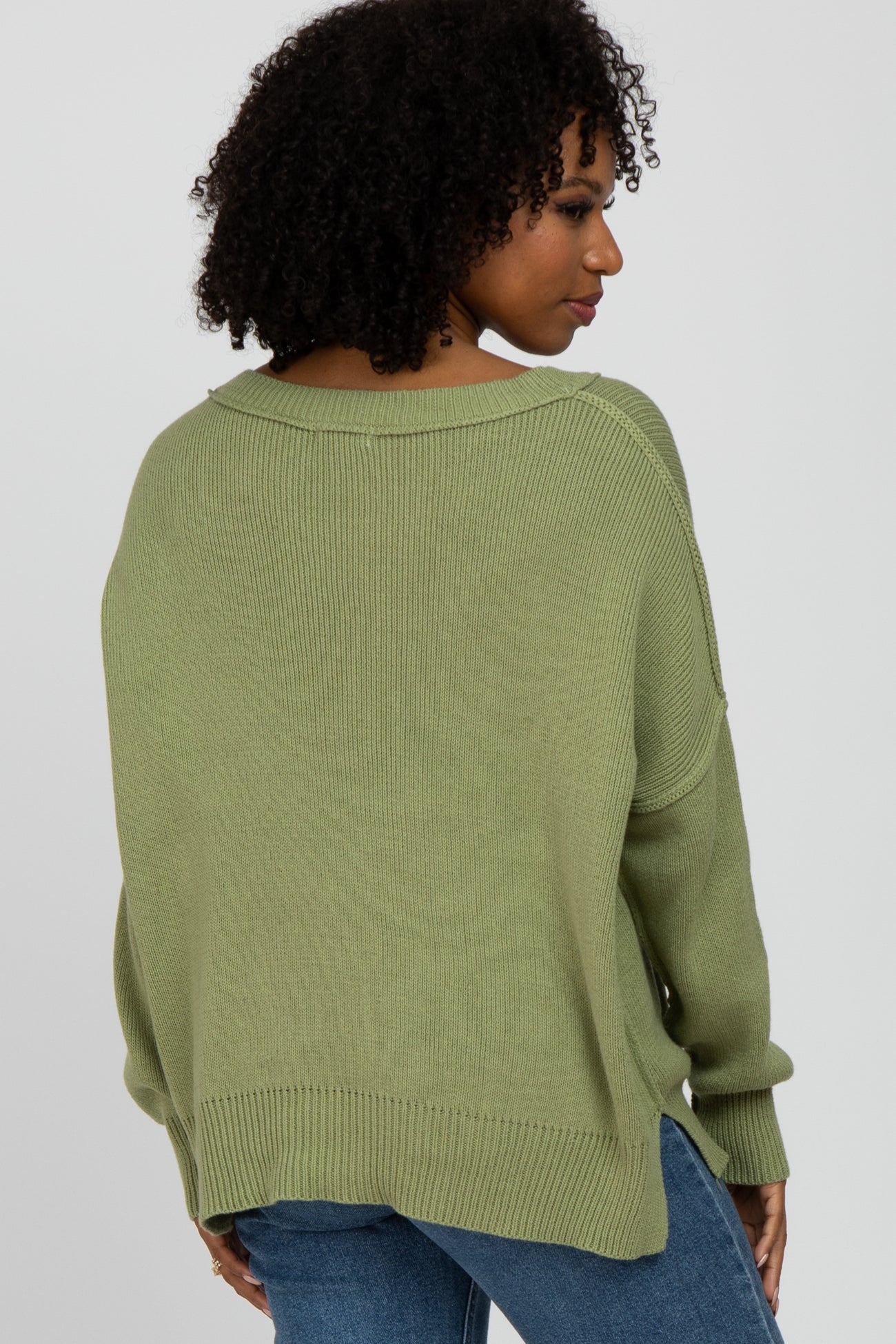 woman wearing a loose-fitting olive green sweater with a wide neckline and a relaxed fit, viewed from the back