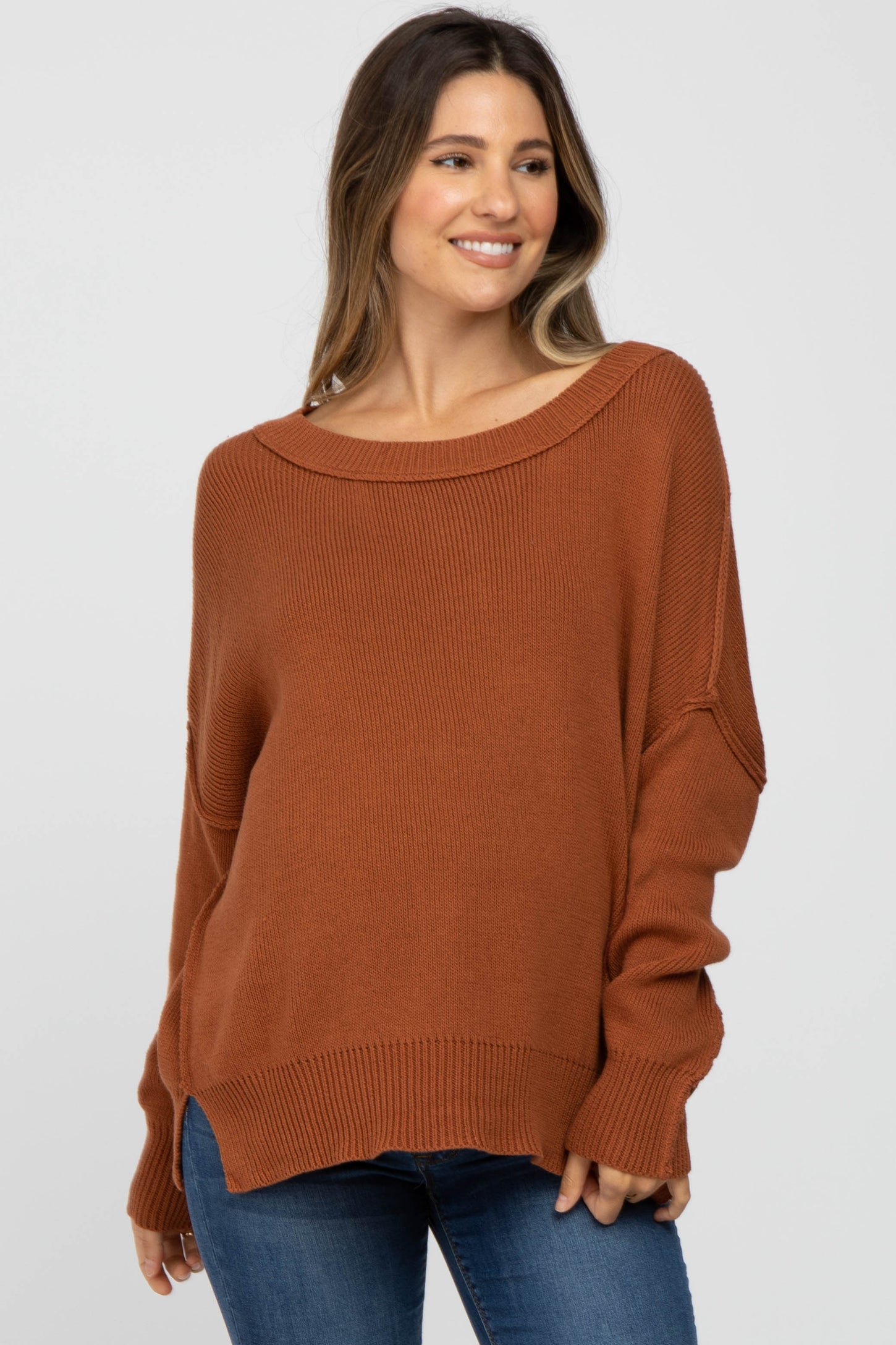 woman wearing a rust-colored oversized maternity sweater with a wide neckline and relaxed fit