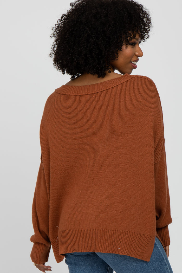 woman wearing a rust oversized sweater with a wide neckline and ribbed texture, shown from the back