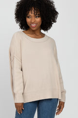 woman wearing a beige oversized sweater with a wide neckline and relaxed fit, paired with blue jeans