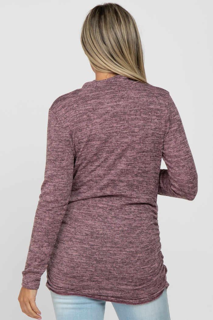 woman wearing a maroon long sleeve maternity top with a relaxed fit and ruched sides, styled with light blue jeans