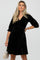woman wearing a black velvet maternity dress with three-quarter sleeves and holding a small clutch bag