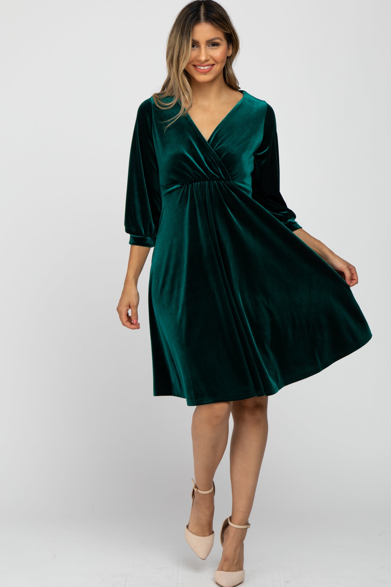 woman wearing a dark green velvet wrap dress with three-quarter sleeves and a flared skirt