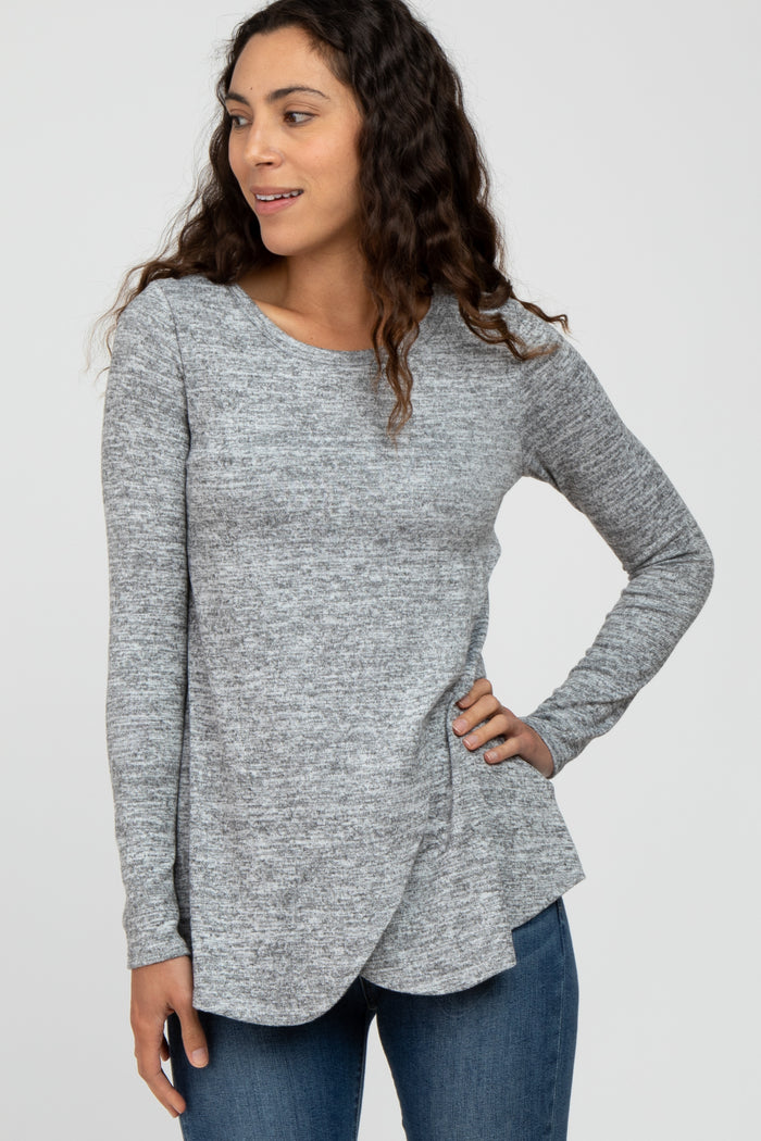 woman wearing a gray long sleeve top with a curved hem and textured fabric, paired with blue jeans