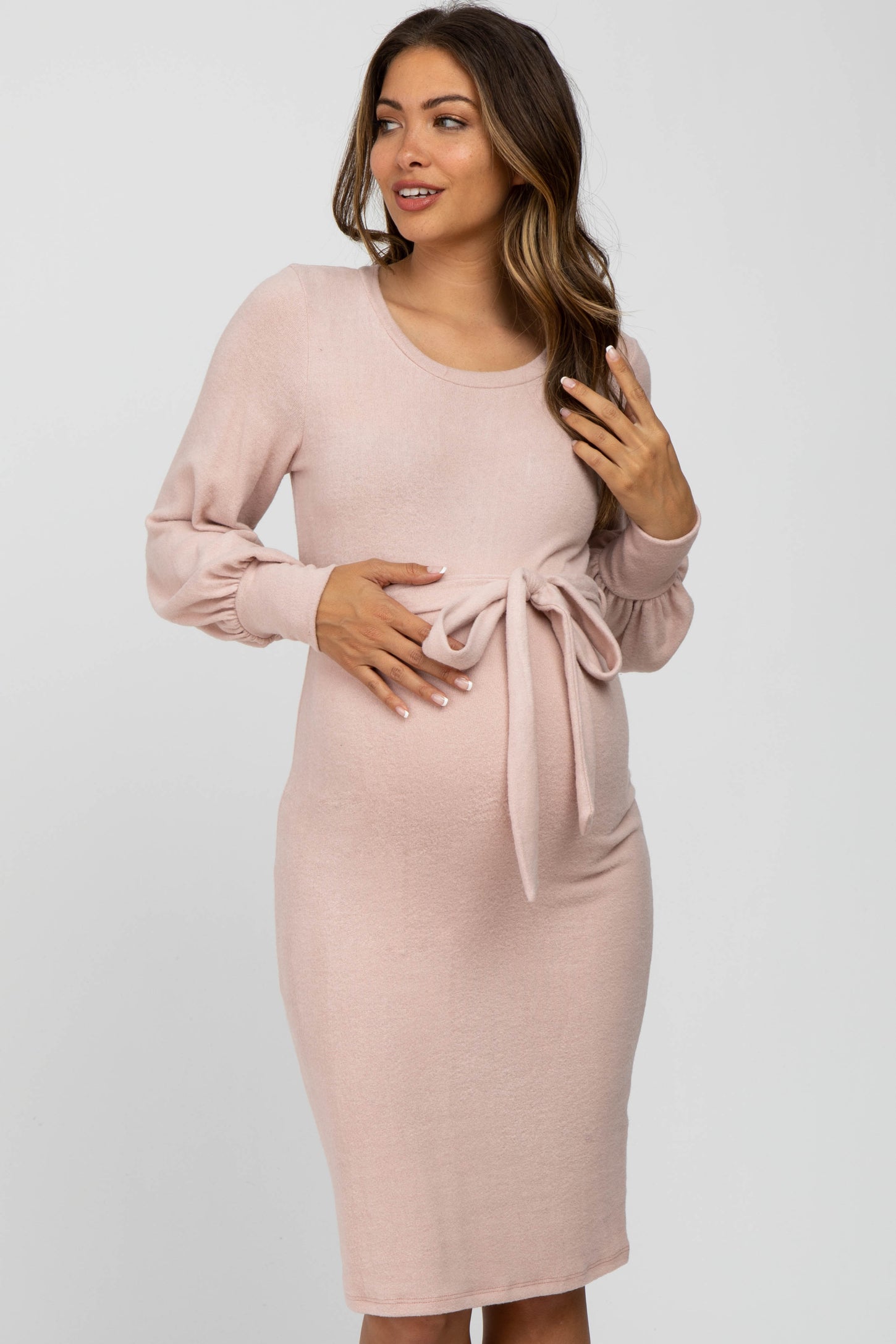 woman wearing a light pink long sleeve maternity dress with a tie detail at the waist and visible baby bump
