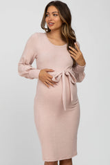 woman wearing a light pink long sleeve maternity dress with a tie detail at the waist and visible baby bump