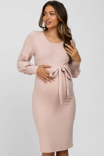 woman wearing a light pink long sleeve maternity dress with a tie detail at the waist and visible baby bump