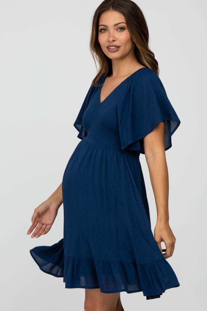 woman wearing a navy blue maternity dress with flutter sleeves and a ruffled hem, showcasing her baby bump