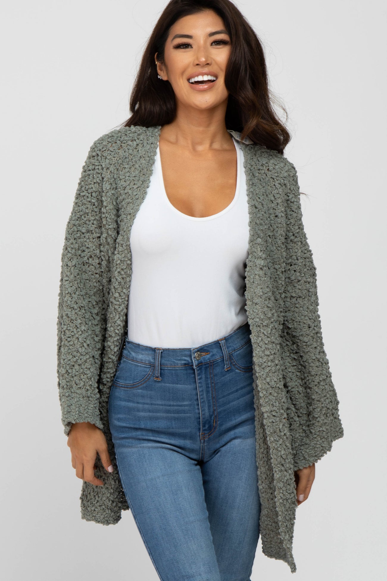 woman wearing a light olive green oversized textured cardigan over a white top and blue skinny jeans