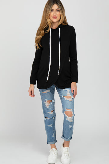 woman wearing a black maternity hoodie with a wrap design, paired with distressed light blue jeans and white sneakers