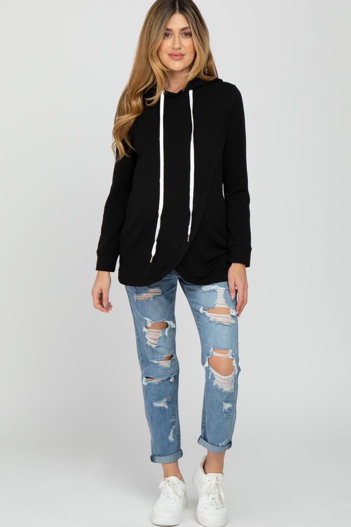 woman wearing a black maternity hoodie with a wrap design, paired with distressed light blue jeans and white sneakers