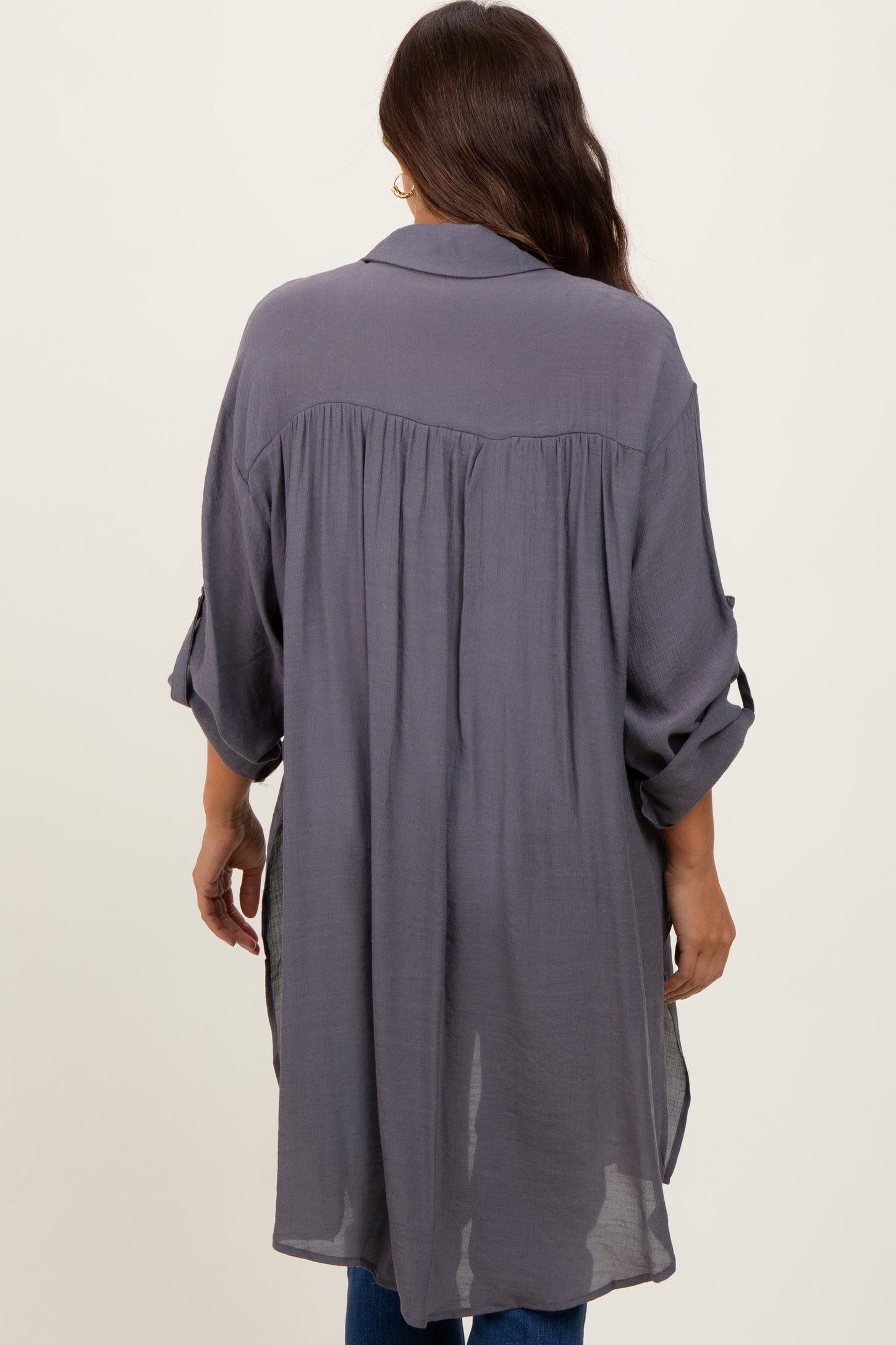 Back view of a woman wearing a long charcoal grey button down tunic shirt with pleated back detail