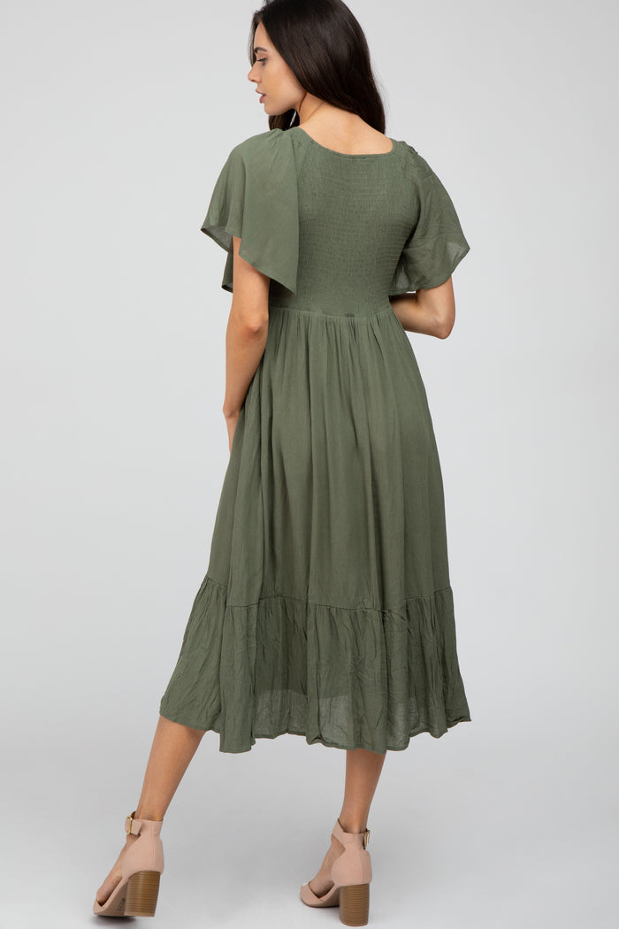 woman wearing a green maternity dress with short flutter sleeves and a tiered ruffle hem, showing a baby bump