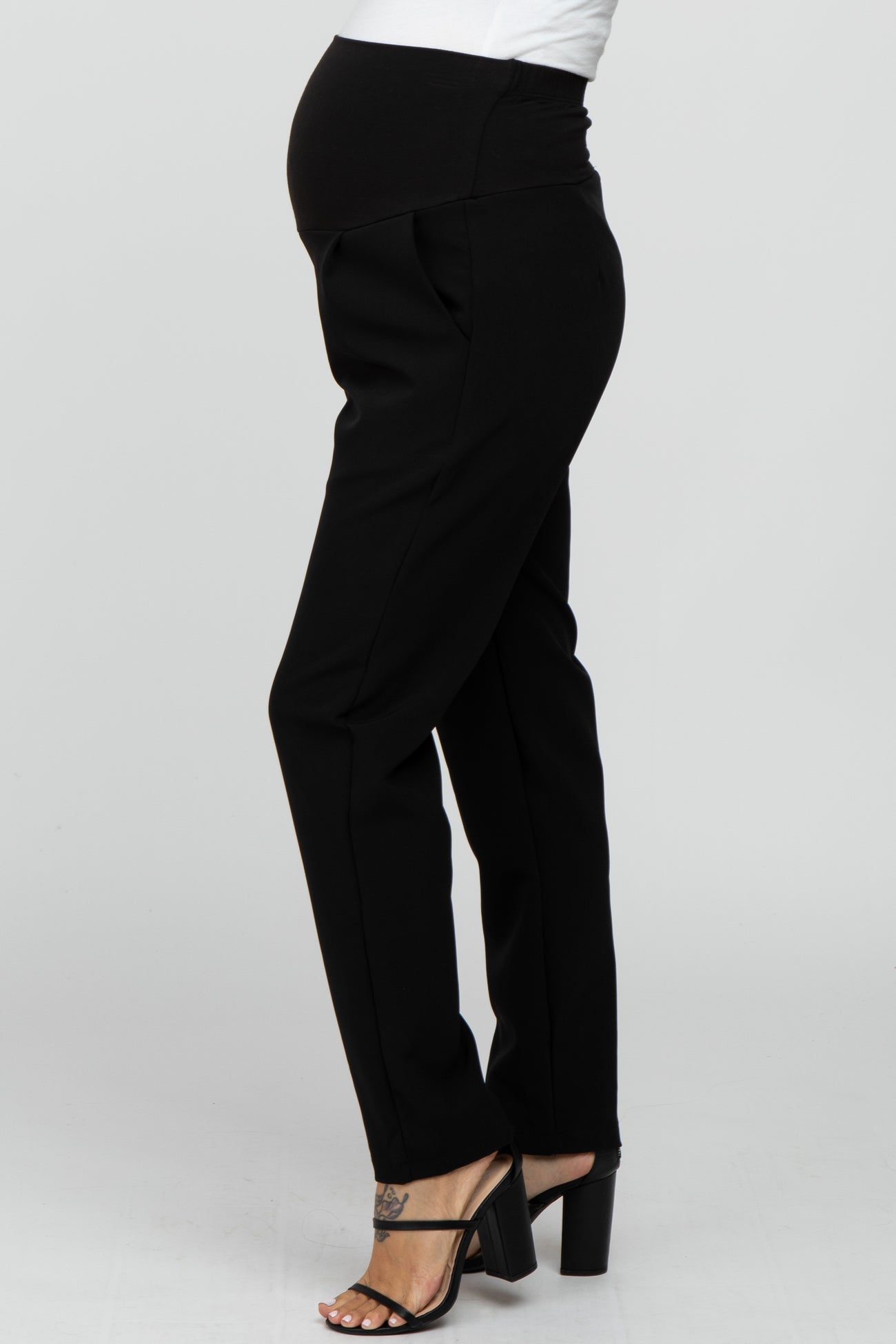 Side view of a pregnant person wearing black maternity dress pants and black high heel sandals