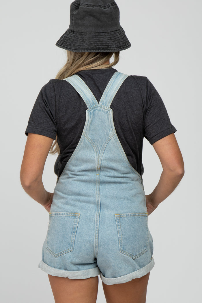woman wearing a black t-shirt and light wash denim maternity overalls, showing back view