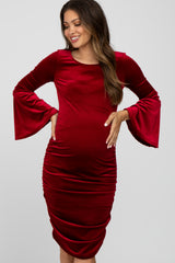 woman wearing a red velvet maternity dress with bell sleeves and gathered side detailing, highlighting her baby bump