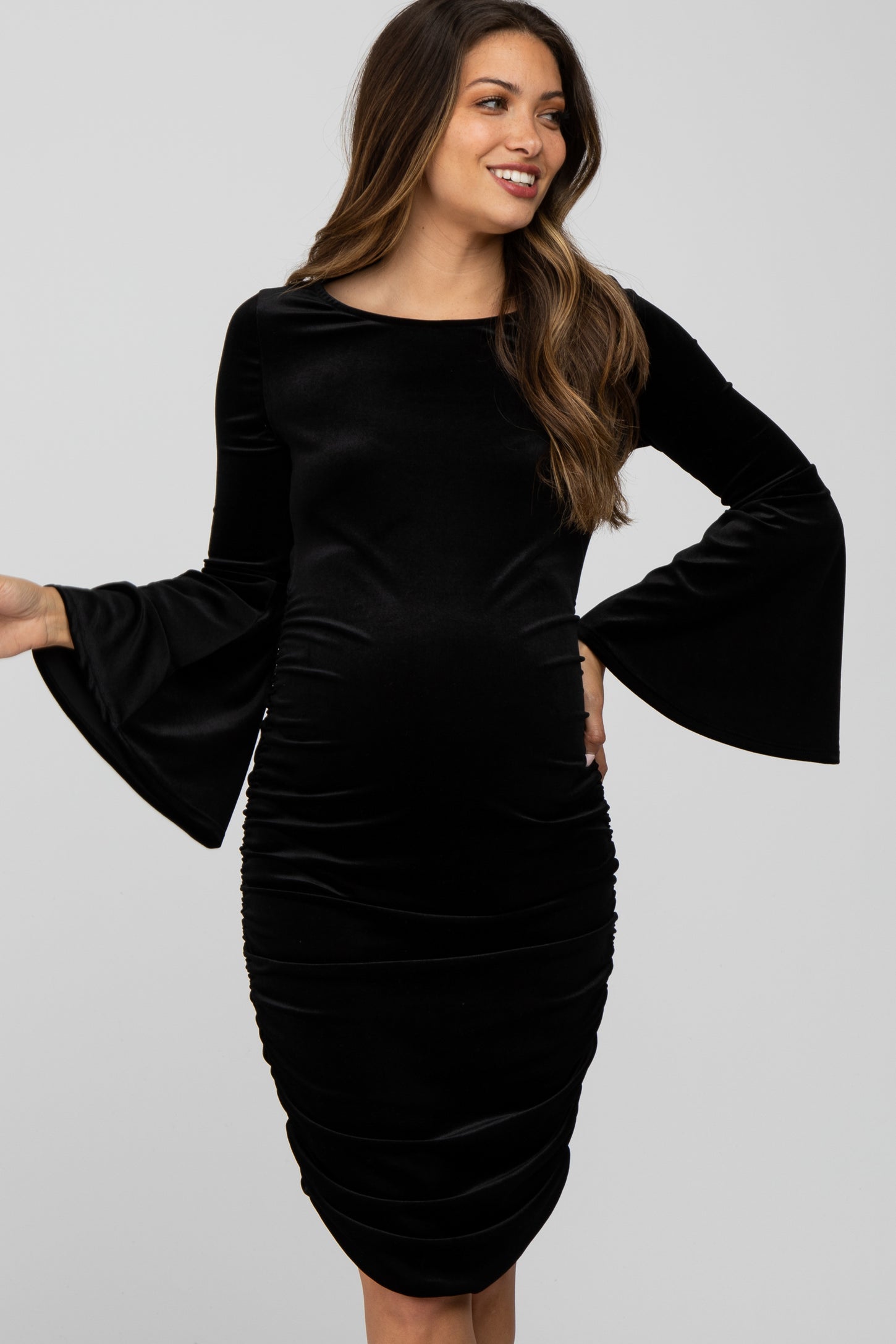 woman wearing a black velvet long sleeve maternity dress with bell sleeves and a visible baby bump