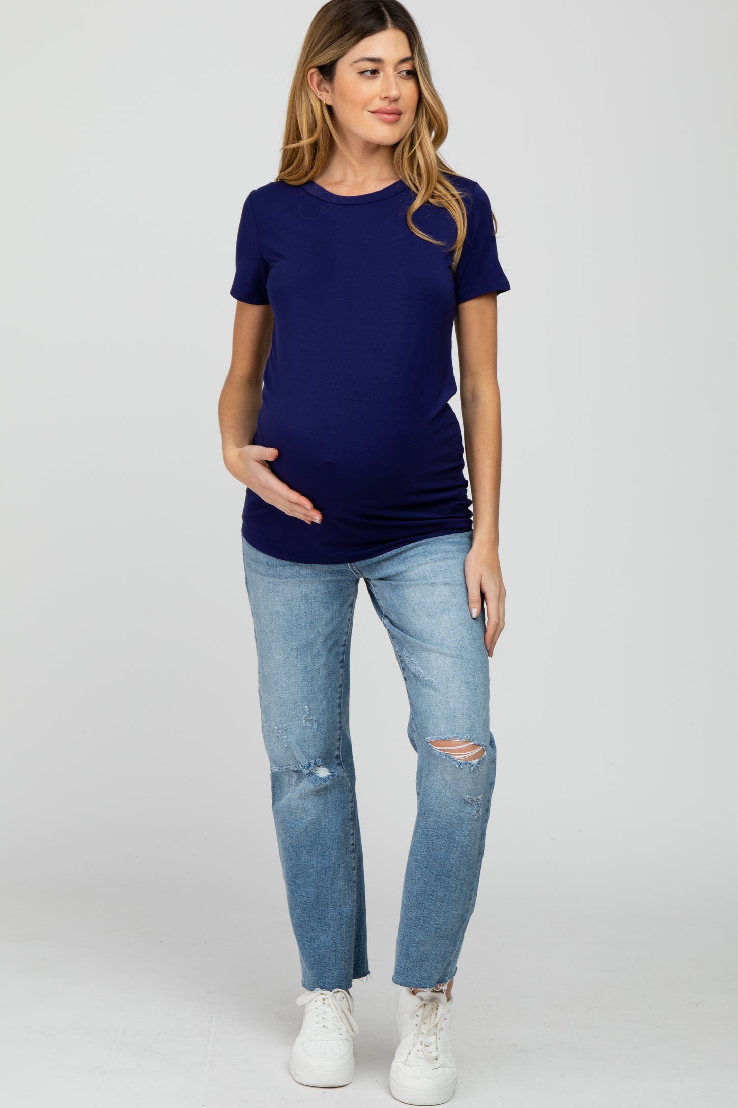 woman wearing a navy blue short sleeve maternity top and distressed light wash jeans, with her baby bump visible