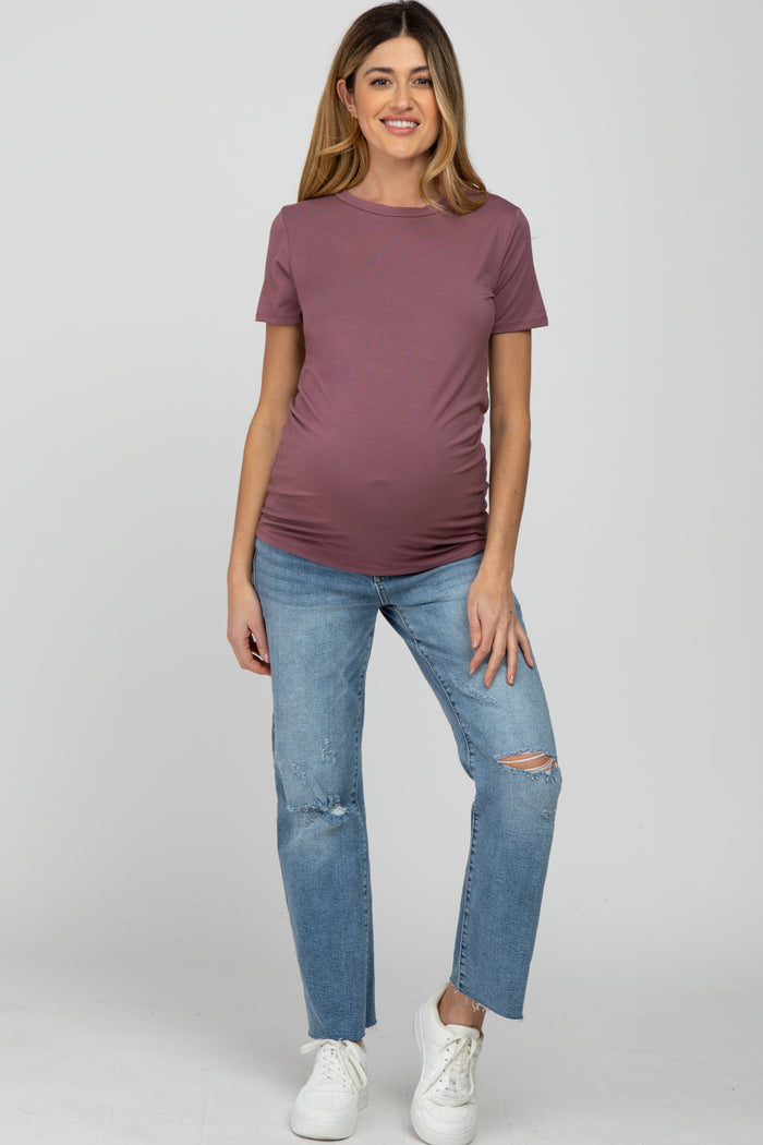 woman wearing a mauve short sleeve maternity top and distressed blue jeans, showing her baby bump