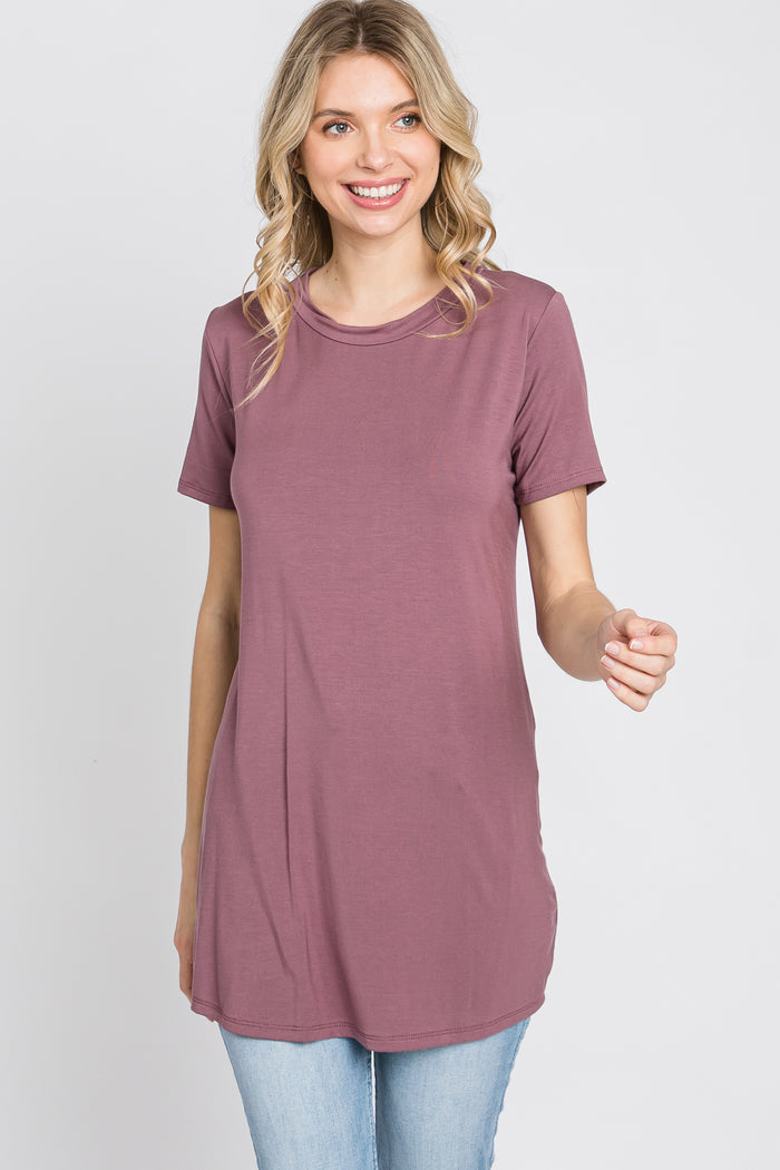 woman wearing a mauve short sleeve tunic top and light wash jeans against a white background