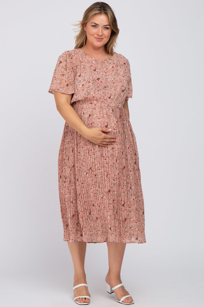 woman wearing a pink floral pleated maternity dress and gently cradling her baby bump