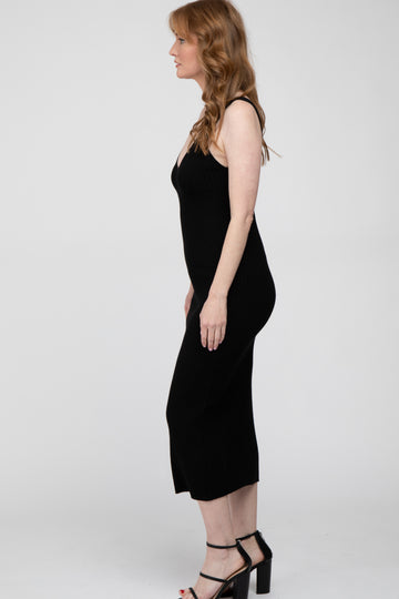 Woman with wavy red hair wearing a sleeveless black ribbed midi dress and black strappy heels