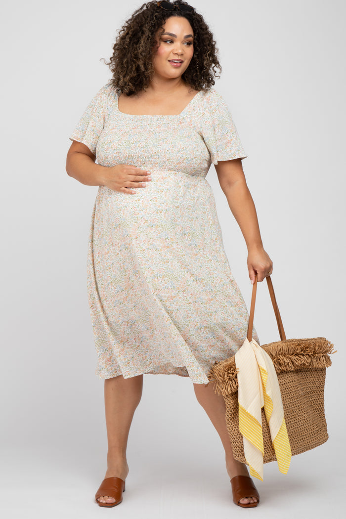 woman wearing a floral print maternity dress with a square neckline and short sleeves, holding a bag and showing her baby bump
