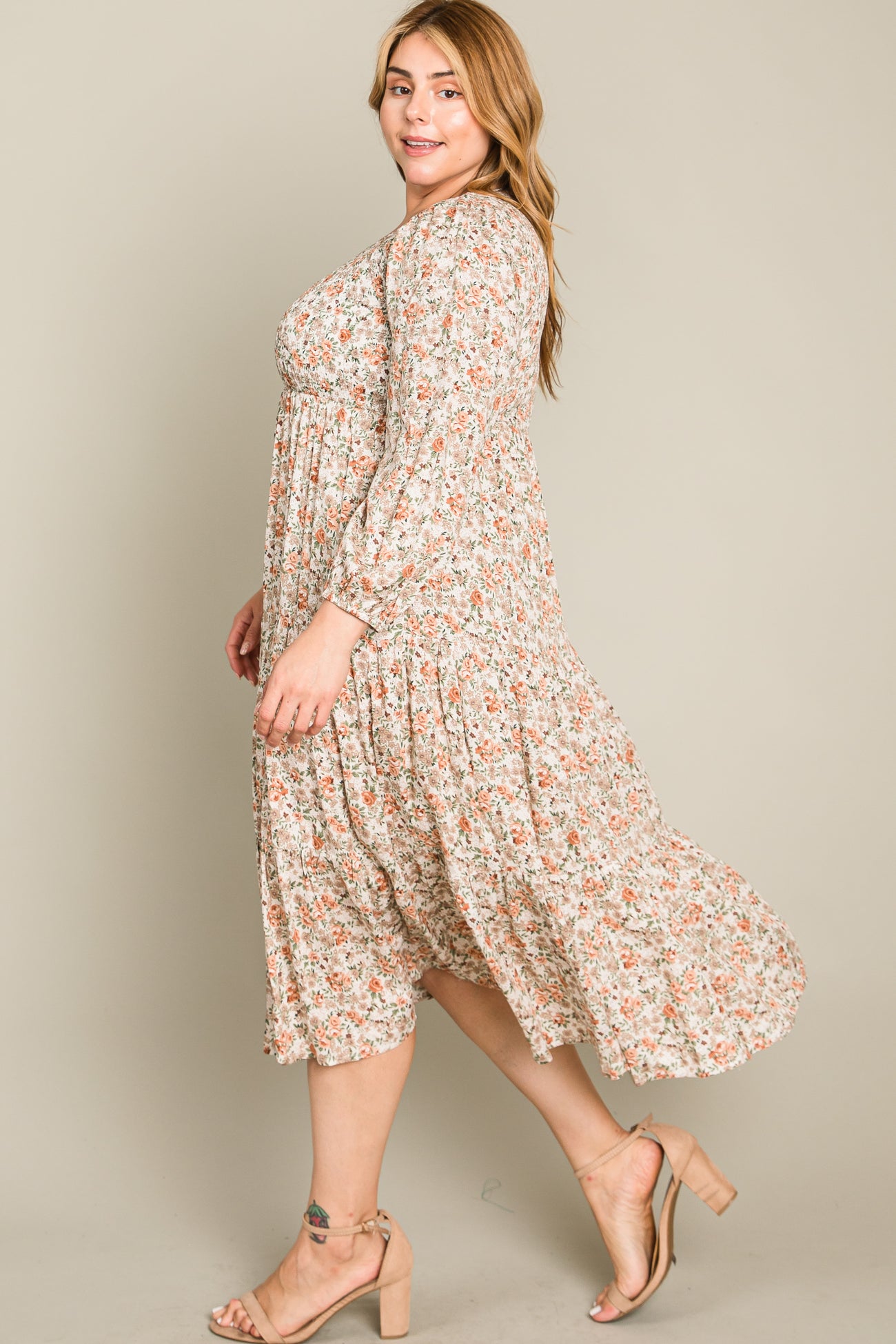 woman wearing a cream floral plus size midi dress with long sleeves and a tiered skirt, smiling while standing in profile