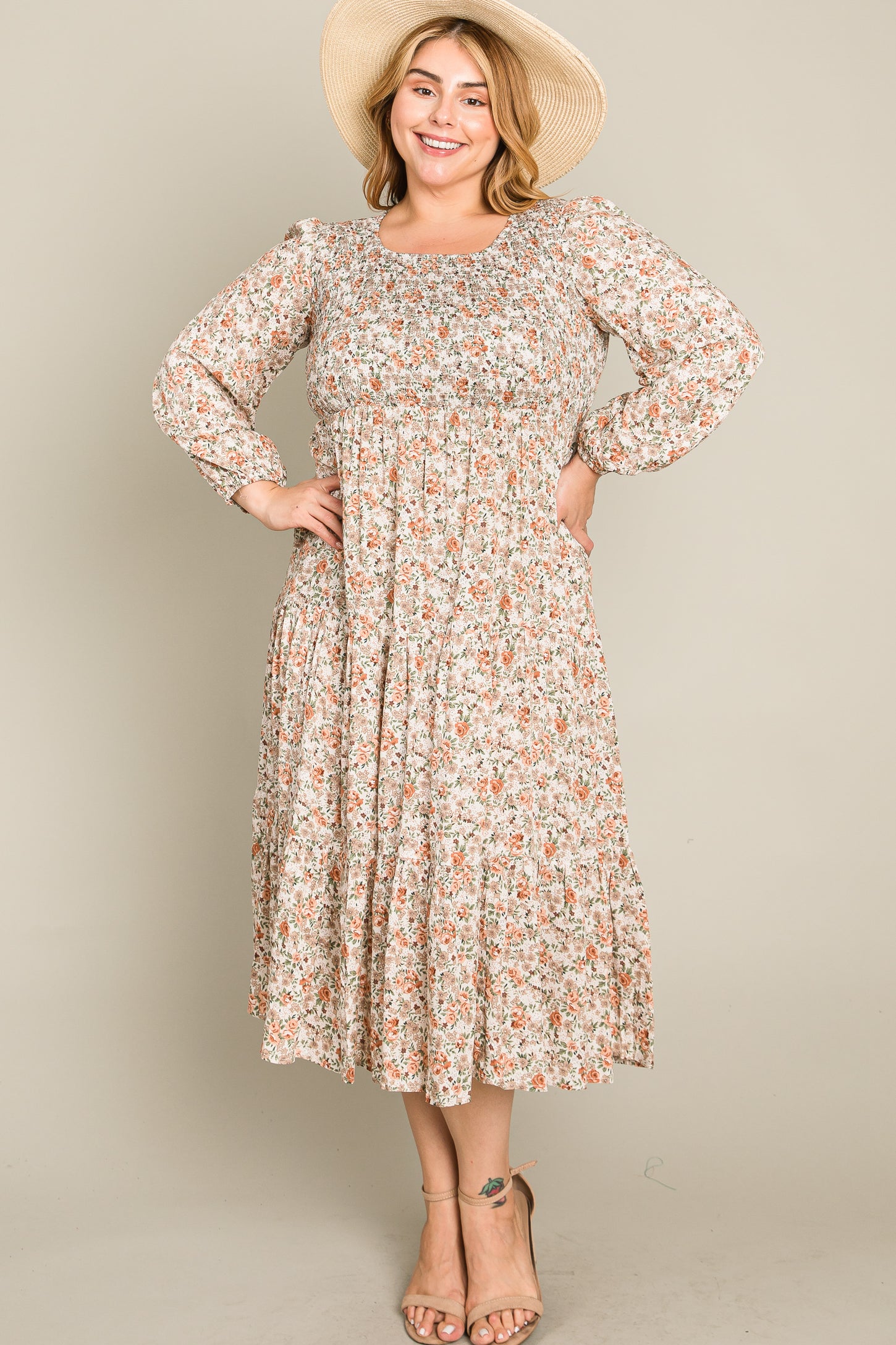 woman wearing a floral printed plus size midi dress with long sleeves and a tiered skirt, accessorized with a wide-brimmed hat