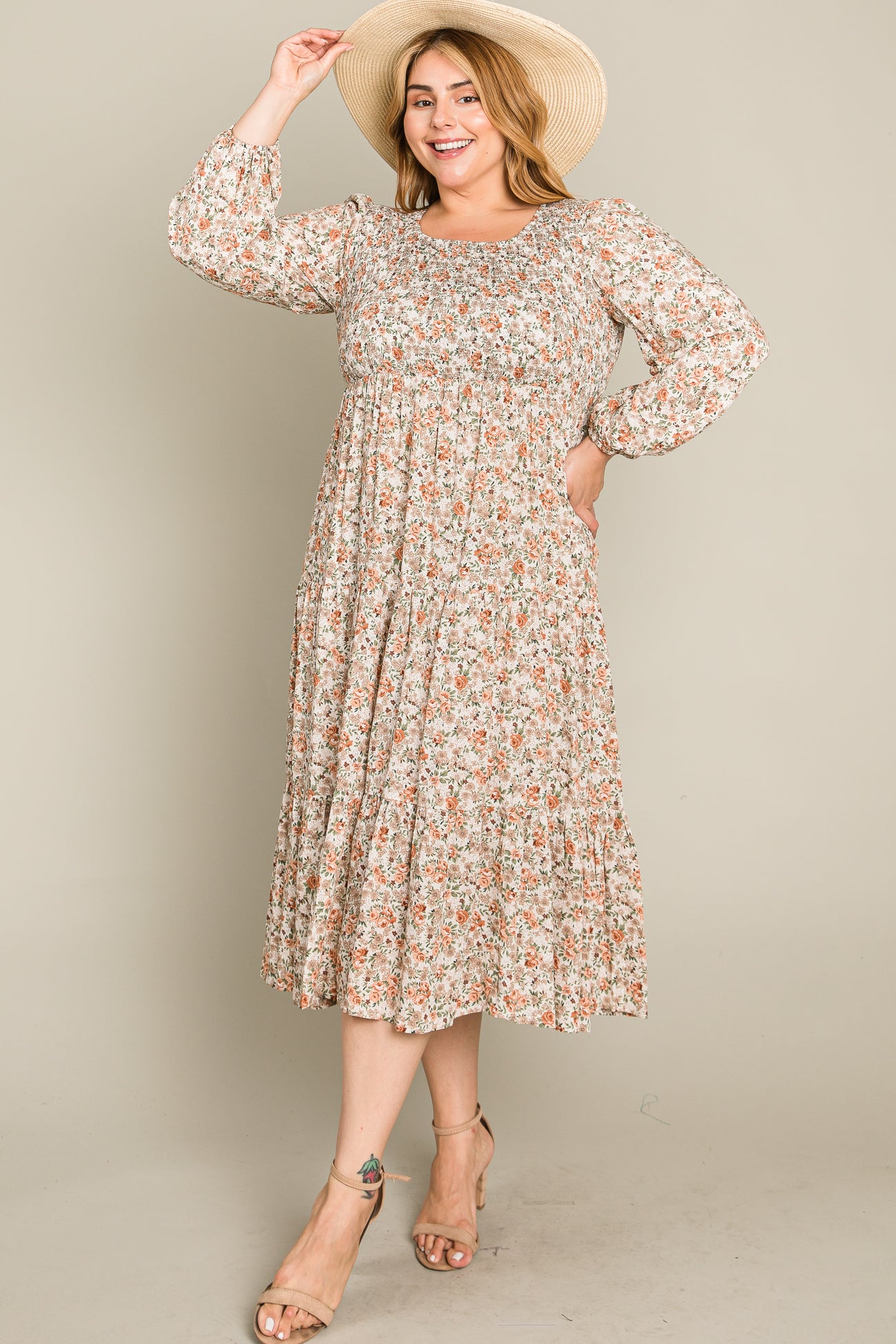 woman wearing a floral print mid-length dress with long sleeves and a fitted bodice, accessorized with a wide-brim hat