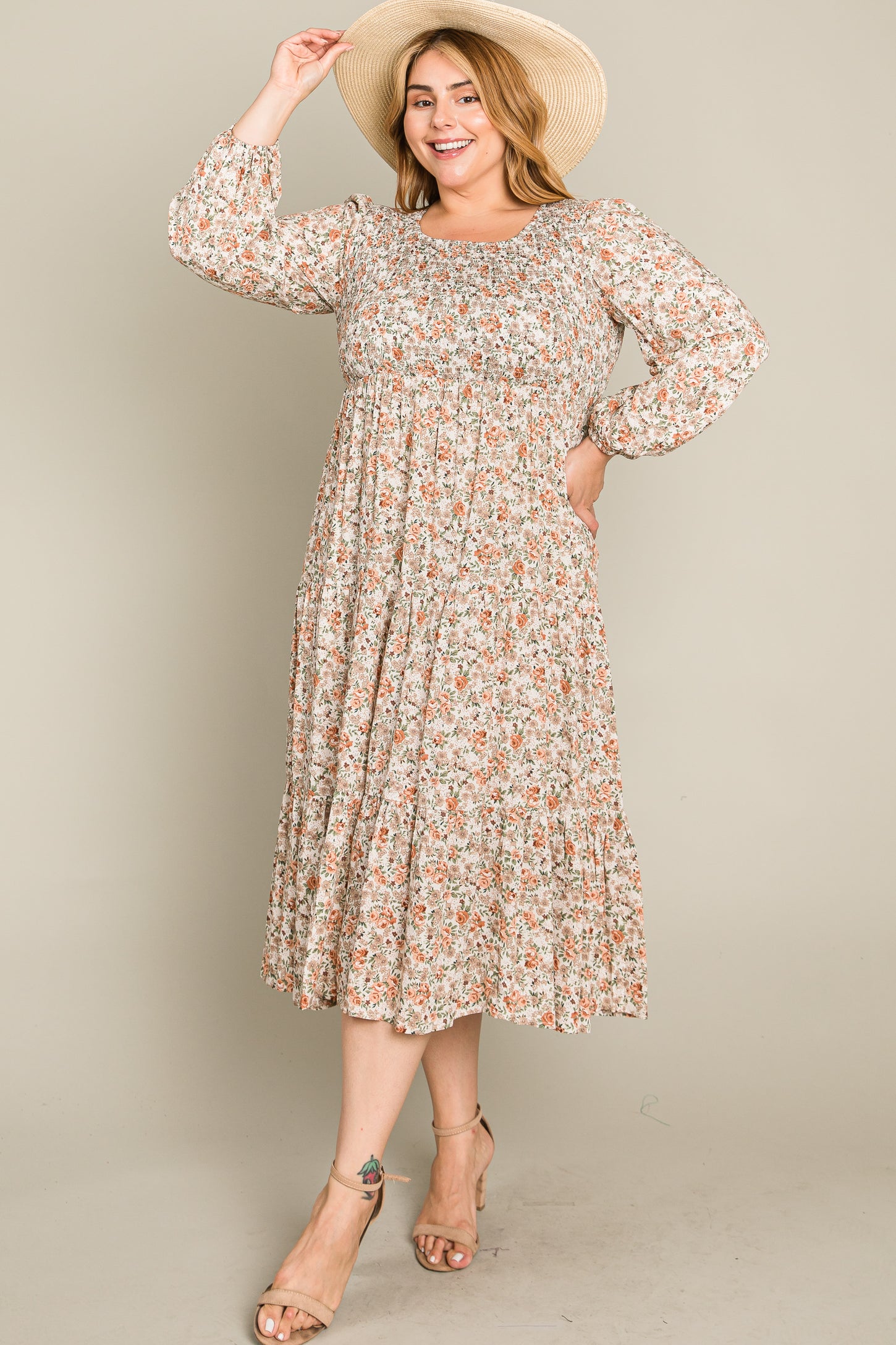 woman wearing a floral print mid-length dress with long sleeves and a fitted bodice, accessorized with a wide-brim hat