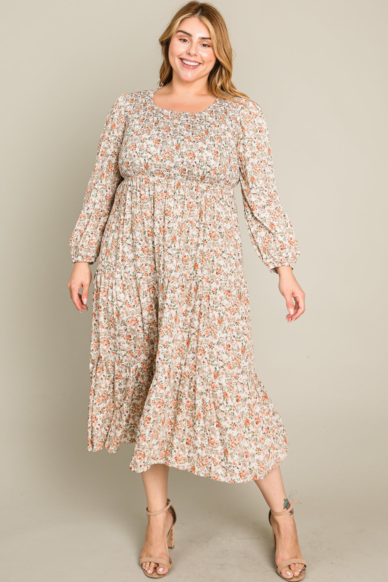woman wearing a beige floral plus size midi dress with long sleeves and a smocked bodice, standing and smiling