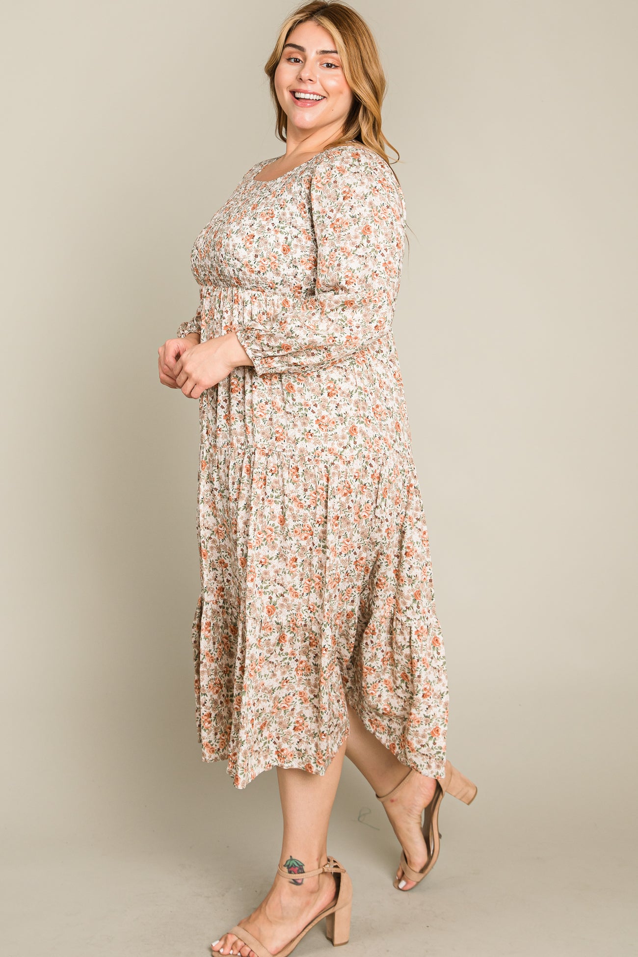 woman wearing a floral plus size midi dress with long sleeves and a tiered skirt, smiling while standing sideways