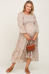 woman wearing a floral long sleeve maternity dress and holding her baby bump with a small brown handbag