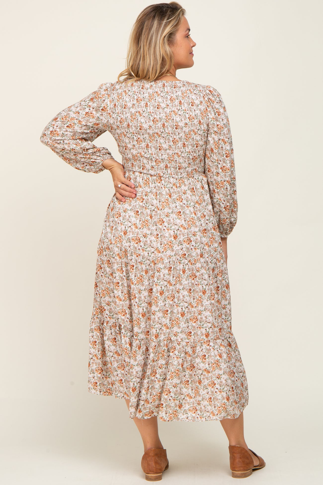 Woman from behind wearing a long sleeve floral smocked midi dress with tiered skirt and brown flats