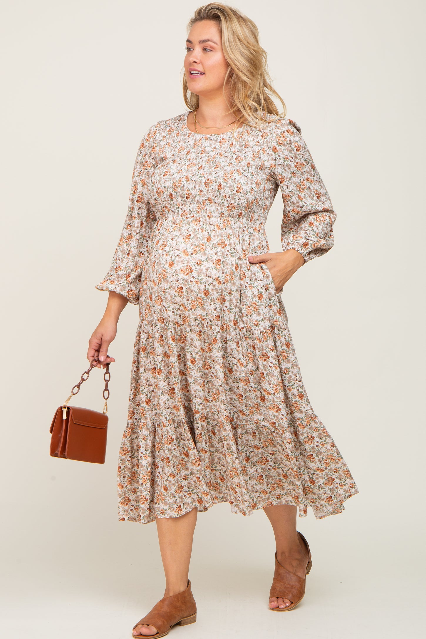 woman wearing a floral print maternity dress with a tiered skirt and bell sleeves, holding a brown handbag and showing baby bump