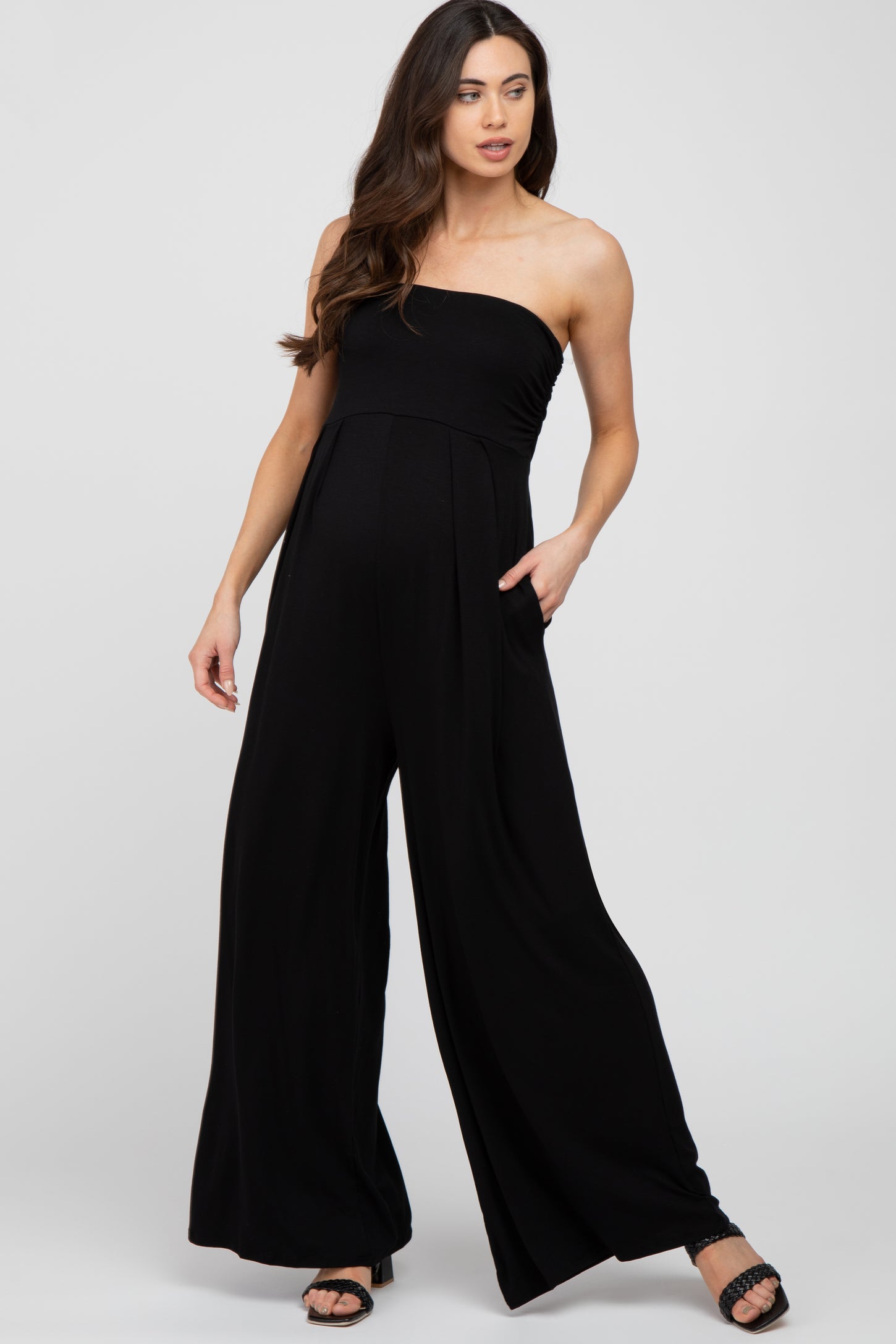 woman wearing a black strapless maternity jumpsuit with wide legs and pockets and showcasing her baby bump