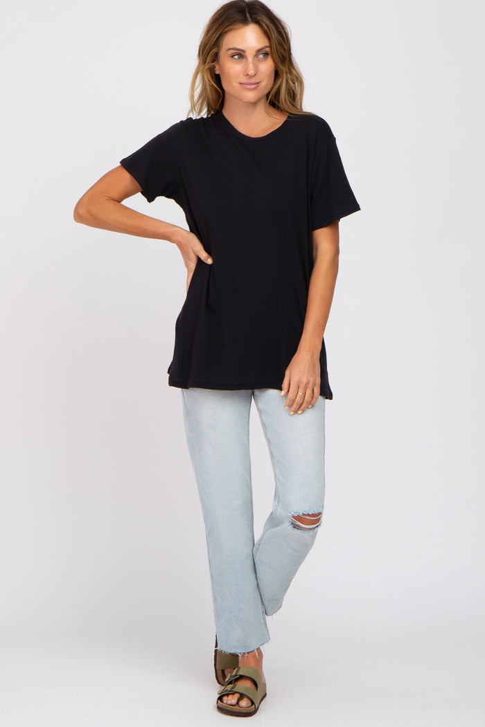 woman wearing a black short sleeve t-shirt and light blue distressed jeans, standing with one hand on her hip