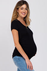 woman wearing a black short sleeve maternity top and showing her baby bump, paired with light blue jeans