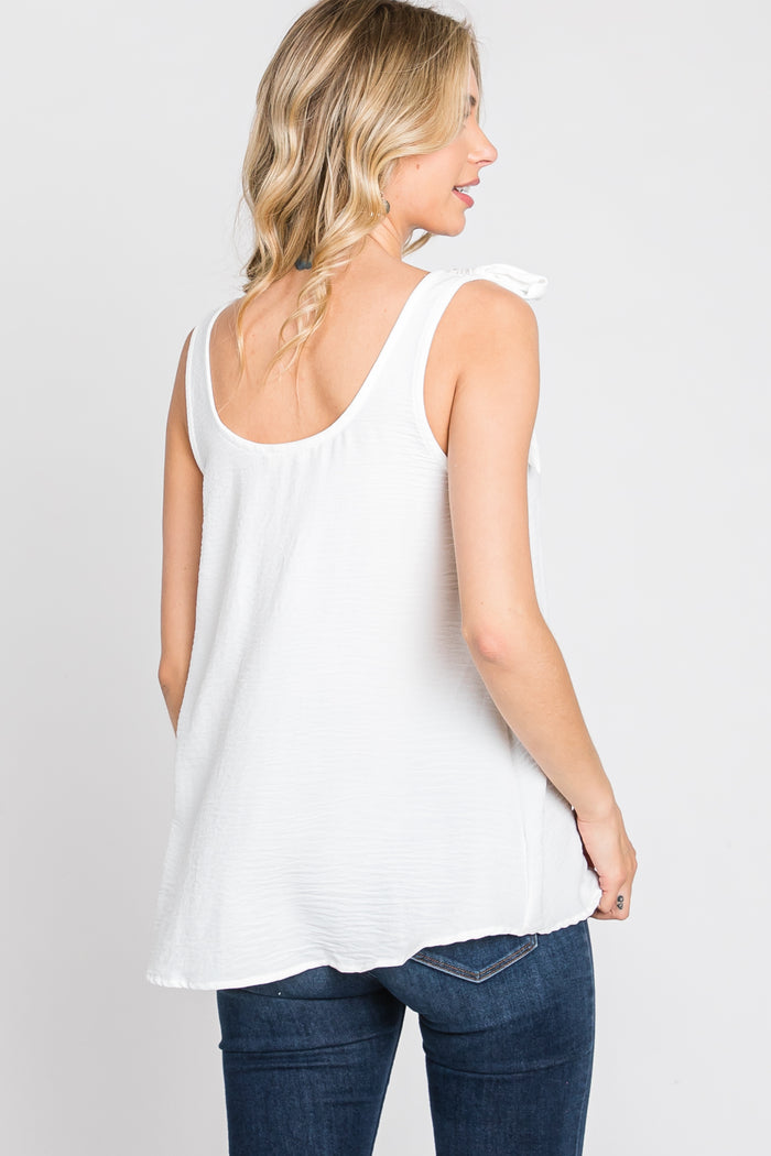 woman wearing a white sleeveless top with a bow detail on one shoulder and blue jeans, viewed from the back