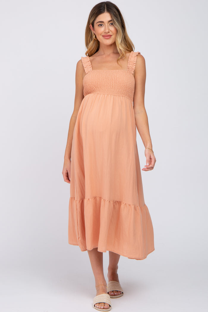 woman wearing a peach maternity dress with frill straps and a flowing skirt, showcasing her baby bump
