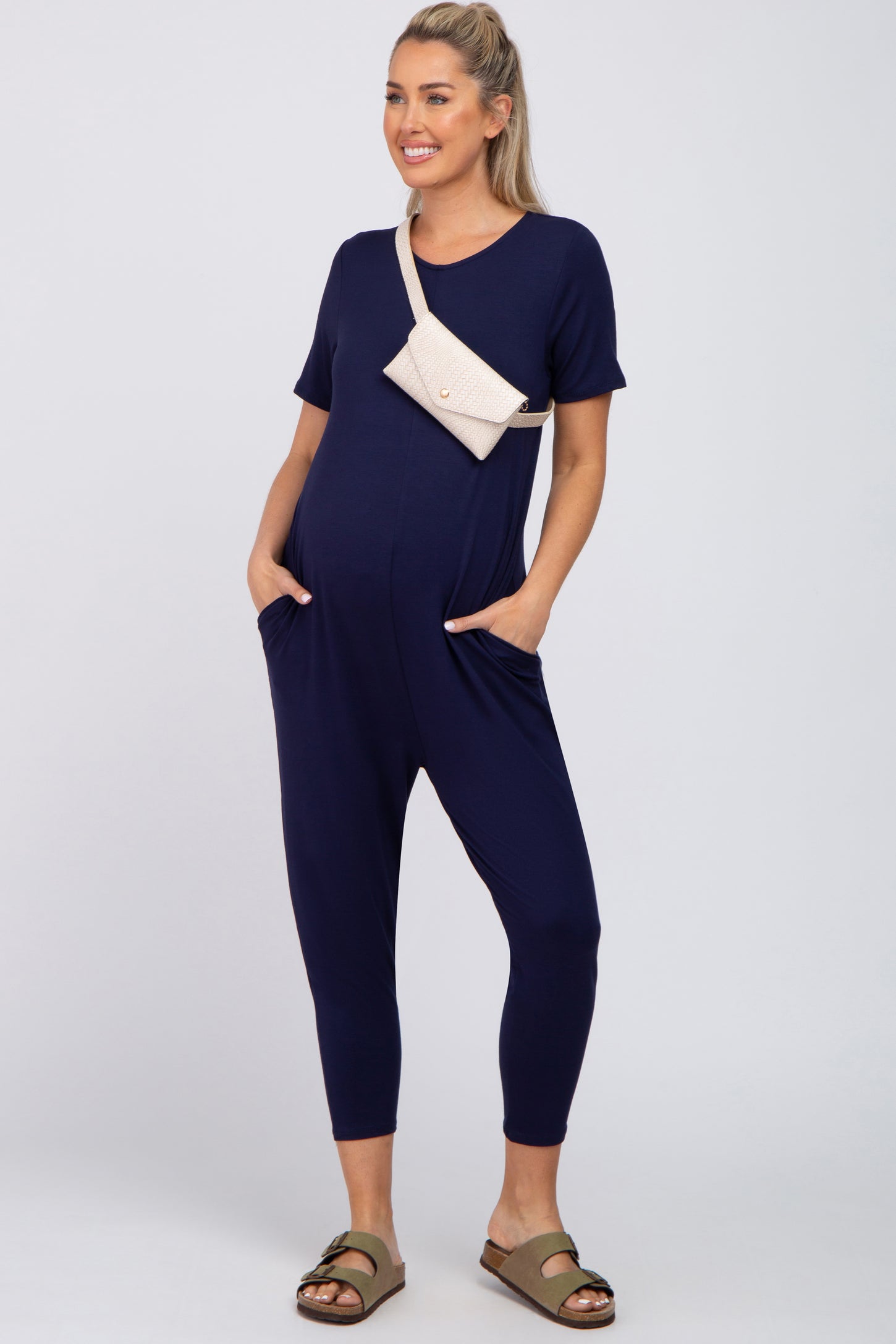woman wearing a navy blue short sleeve maternity jumpsuit with pockets and a crossbody bag, styled comfortably