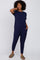 woman wearing a navy blue short sleeve jumpsuit with side pockets and relaxed fit sandals